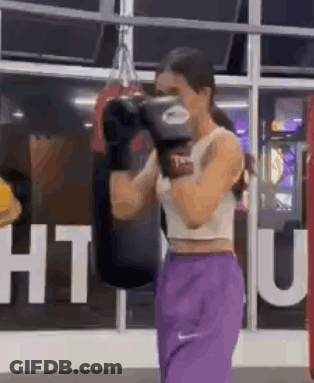 A Woman Is Wearing Boxing Gloves And Purple Pants In A Gym . GIF