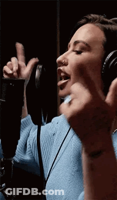 A Woman Is Wearing Headphones And Singing Into A Microphone . GIF