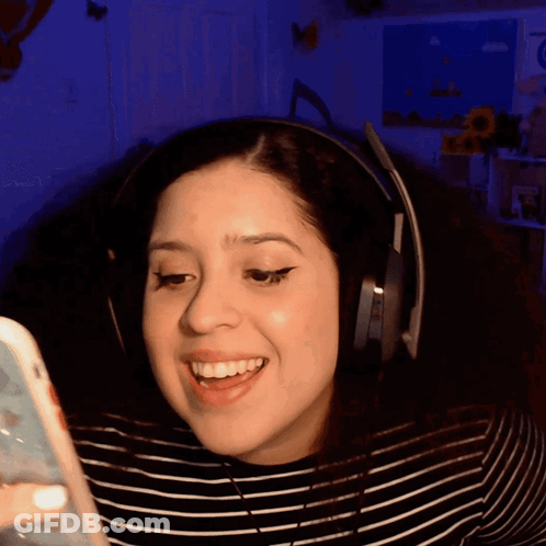 A Woman Is Wearing Headphones And Smiling While Looking At Her Phone GIF