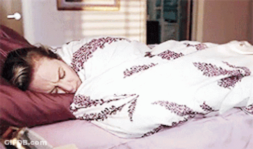 A Woman Is Wrapped In A Blanket And Sleeping On A Bed GIF