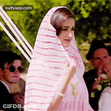 A Woman Is Wrapped In A Pink And White Striped Shawl . GIF