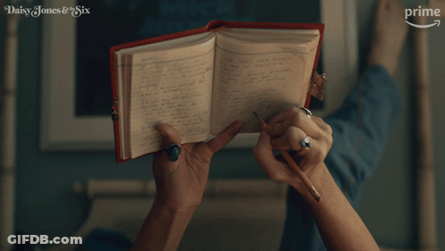 A Woman Is Writing In A Notebook With The Words Daisy Jones & Six On The Bottom Right GIF