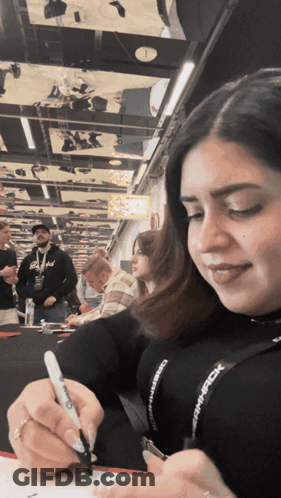 A Woman Is Writing On A Piece Of Paper With A Sharpie Marker While Wearing A Lanyard That Says Dmpack GIF