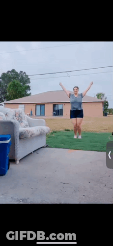 A Woman Jumping In The Air In Front Of A House GIF