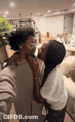 A Woman Kissing Another Woman 'S Neck In A Living Room GIF