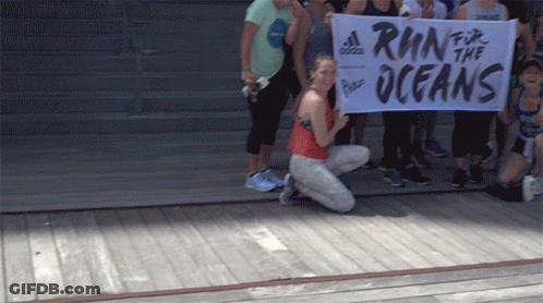 A Woman Kneeling Down Holding A Banner That Says Run For The Oceans GIF