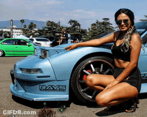 A Woman Kneeling In Front Of A Car With Rays Written On The Side GIF