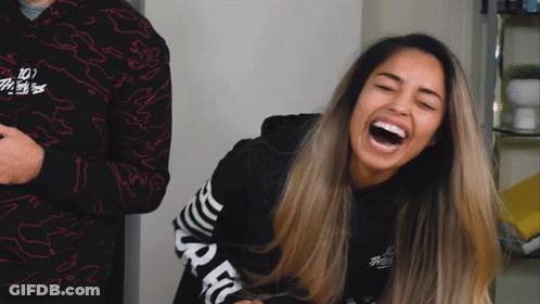 A Woman Laughs While Wearing A Black Shirt With The Word Spec On The Sleeves GIF