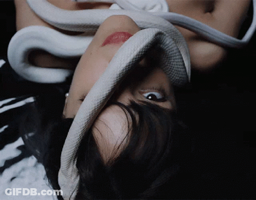 A Woman Laying Down With A Snake Around Her Face GIF