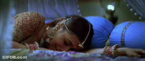 A Woman Laying On A Bed With A Blue Pillow Behind Her GIF