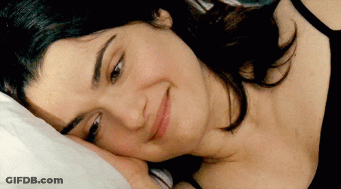 A Woman Laying On A Bed With Her Head On A Pillow And Smiling GIF