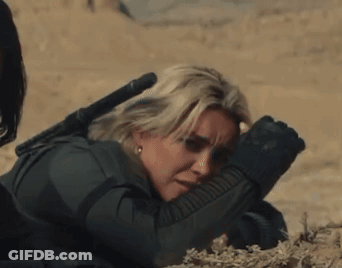 A Woman Laying On The Ground With A Rifle In Her Hand GIF