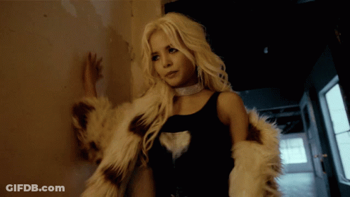 A Woman Leaning Against A Wall Wearing A Fur Coat And A Choker GIF