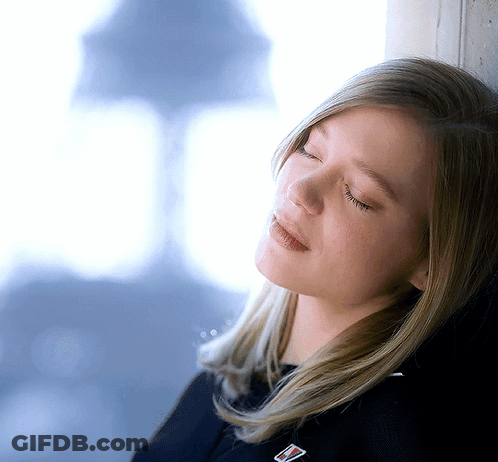 A Woman Leaning Against A Wall With Her Eyes Closed And A Badge On Her Shirt That Says ' Tommy Hilfiger ' GIF