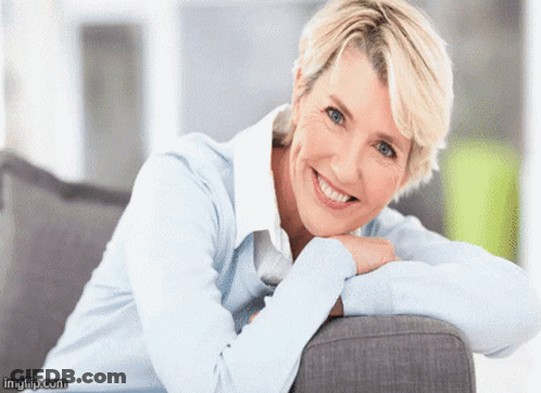 A Woman Leaning On A Couch With Her Head Resting On Her Hand And Smiling GIF