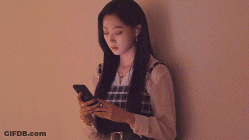 A Woman Leans Against A Wall Looking At Her Phone GIF