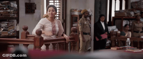 A Woman Leans On A Railing In A Courtroom While A Police Officer Stands In The Background GIF