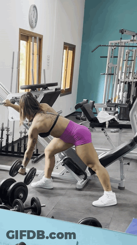 A Woman Lifting A Dumbbell In A Gym With A Clock On The Wall GIF