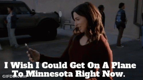 A Woman Looking At Her Phone With The Words " I Wish I Could Get On A Plane To Minnesota Right Now " Above Her GIF