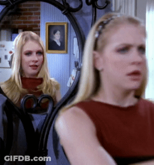 A Woman Looking At Herself In A Mirror With A Picture Of A Woman On The Wall Behind Her GIF