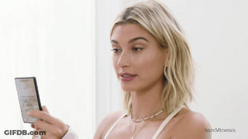 A Woman Looking At Herself In A Mirror With Bareminerals Written On The Bottom Right GIF