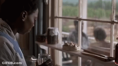 A Woman Looking Out Of A Window With A Glass In Her Hand GIF