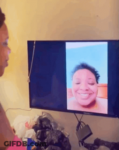 A Woman Looks At A Picture Of Herself On A Tv Screen GIF