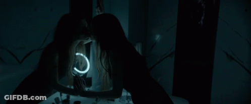 A Woman Looks At Her Reflection In A Mirror With A Light Ring GIF