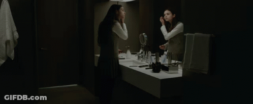 A Woman Looks At Herself In A Bathroom Mirror GIF