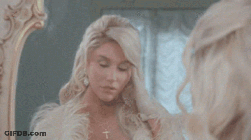 A Woman Looks At Herself In A Mirror And Adjusts Her Hair GIF