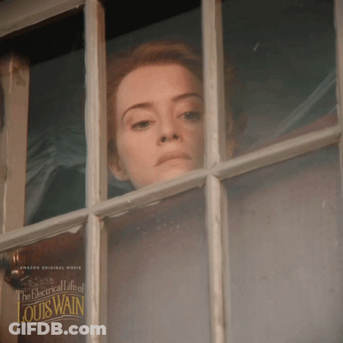 A Woman Looks Out A Window With A Poster For The Electrical Life Of Louis Wain GIF