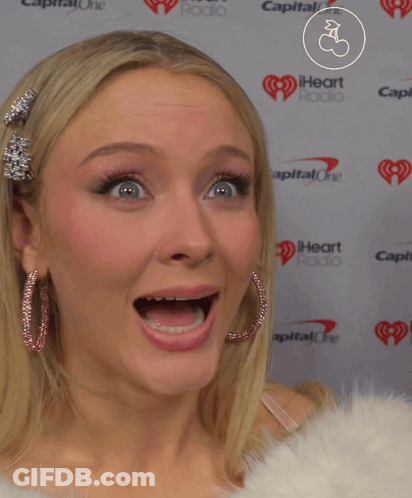 A Woman Making A Funny Face In Front Of A Wall That Says Capital One GIF