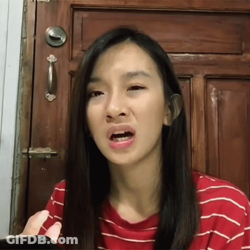 A Woman Making A Funny Face While Holding A Cell Phone In Front Of A Wooden Door GIF