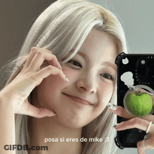 A Woman Making A Heart Shape With Her Hands While Holding A Green Apple GIF