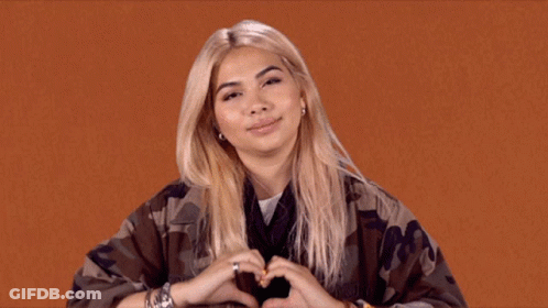 A Woman Making A Heart With Her Hands On An Orange Background GIF
