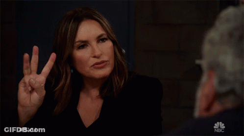 A Woman Making A Peace Sign In Front Of A Man With The Nbc Logo In The Corner GIF