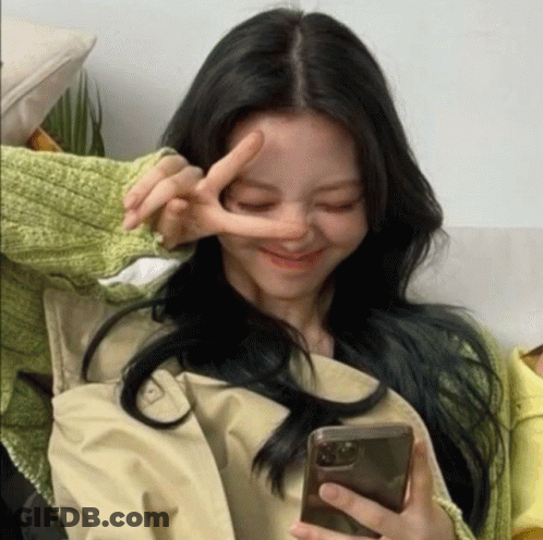 A Woman Making A Peace Sign While Holding A Phone GIF
