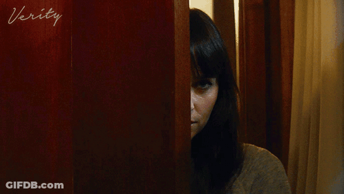 A Woman Peeking Out From Behind A Door With The Word Verity Written On It GIF