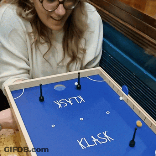 A Woman Playing A Game Called Klask On A Blue Board GIF