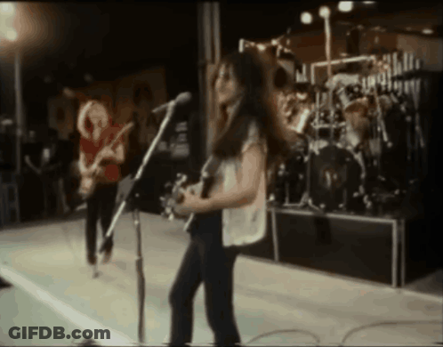 A Woman Playing A Guitar And Singing Into A Microphone On Stage GIF