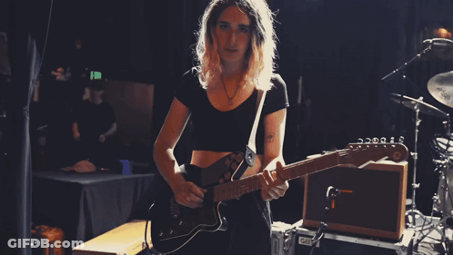 A Woman Playing A Guitar In Front Of A Drum Set GIF