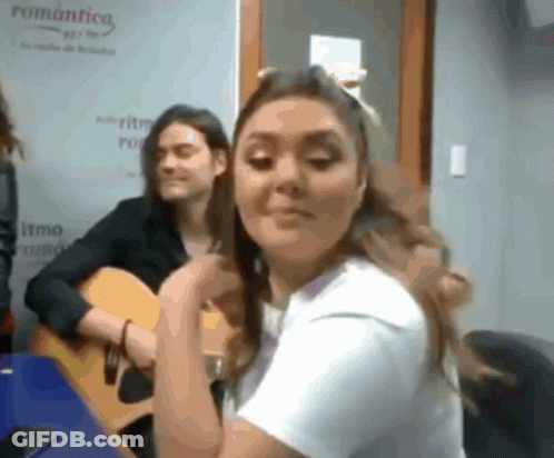 A Woman Playing A Guitar In Front Of A Sign That Says " Romantica " GIF