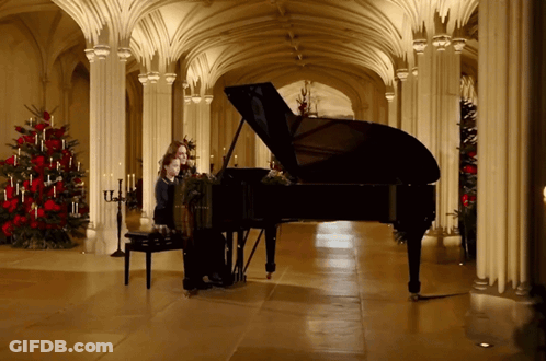 A Woman Playing A Piano In A Hallway With Christmas Trees GIF