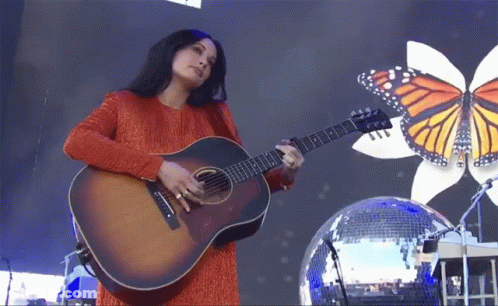 A Woman Playing An Acoustic Guitar In Front Of A Disco Ball GIF