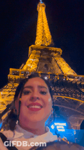 A Woman Poses In Front Of The Eiffel Tower At Night GIF
