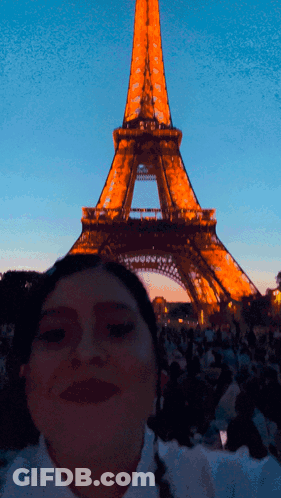 A Woman Poses In Front Of The Eiffel Tower At Night GIF