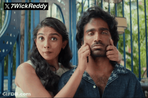 A Woman Putting Her Hand On A Man 'S Face With A 7Wick Reddy Logo In The Background GIF