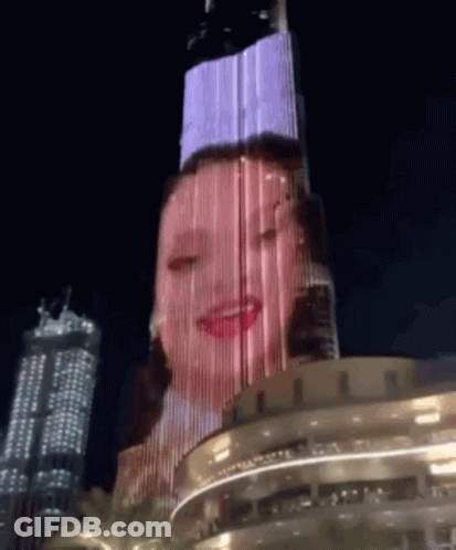 A Woman 'S Face Is Projected On A Building At Night GIF