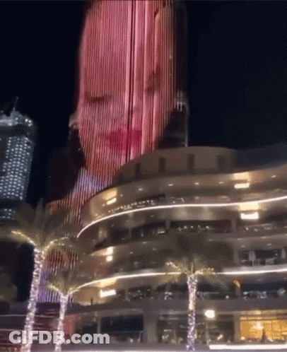A Woman 'S Face Is Projected Onto The Side Of A Building GIF