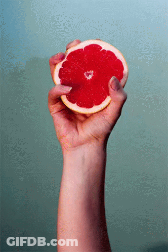 A Woman 'S Hand Is Holding A Slice Of Grapefruit In Her Right Hand GIF